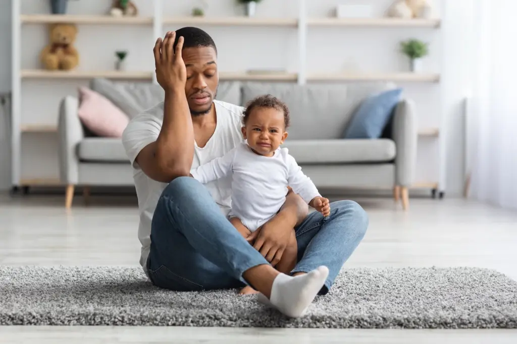 Parental Burnout: Signs, Causes, and How to Recover Your Joy 4 Exhausted father sitting on floor holding a crying baby head in hand
