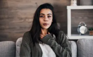 Woman clutching her chest with a worried expression while sitting on a couch 