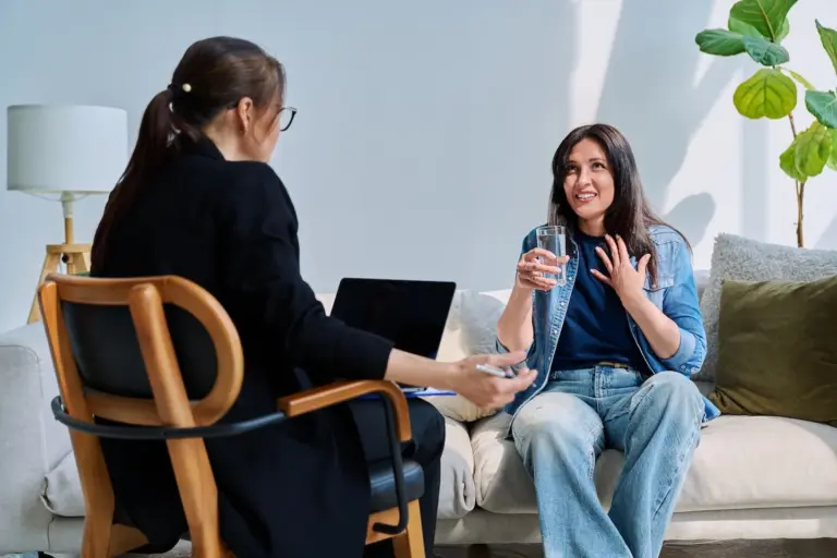 Woman holding a glass of water talks with her therapist during an anxiety therapy session in Austin